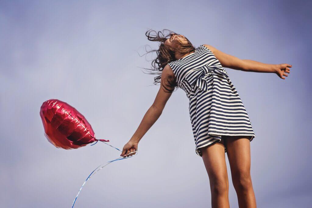 Mulher feliz com o céu ao fundo e um balão de coração, todo cenário representando a Felicidade para começar bem o dia.